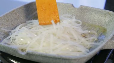 Bir kadın pirinç eriştesi bir tavada ahşap bir spatula ile karıştırma