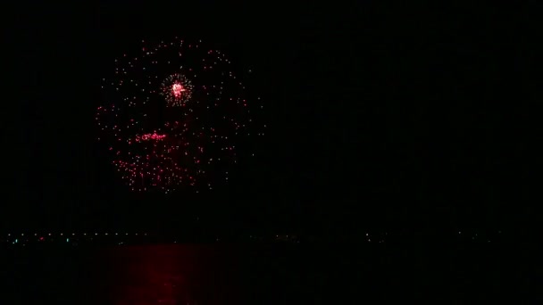 Färgade gnistor av festliga fyrverkerier på natthimlen ovanför floden reflekteras i vattnet. Tid varv — Stockvideo