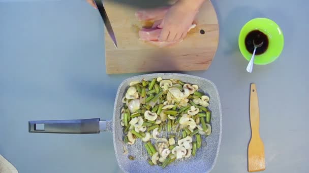 Eine Frau mixt Bohnen und Champignons in einer Pfanne und schneidet die Hühnerbrust. Zeitrunden. — Stockvideo