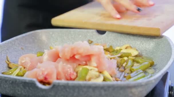 Een vrouw voegt kipfilet in een pan toe aan de bonen en paddestoelen. Tijd ronden — Stockvideo