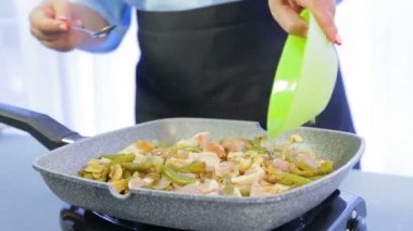 Bir kadın fasulye ve mantar ve soya sosu ile tavuk fileto ile bir tavada ahşap bir spatula karıştırır. Zaman turları