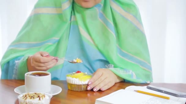 Bir kafede açık yeşil eşarp genç bir Müslüman kadın kek ve içecek çay yiyor — Stok video