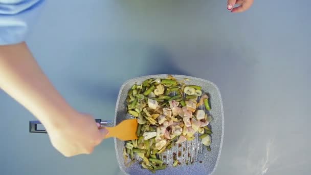 A woman mixes with a wooden spatula beans and mushrooms roasting in a pan with chicken pieces with soy sauce — Stock Video