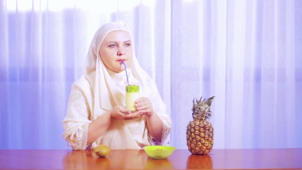 Une jeune femme musulmane dans une écharpe légère boit un smoothie aux fruits d'une paille . — Video