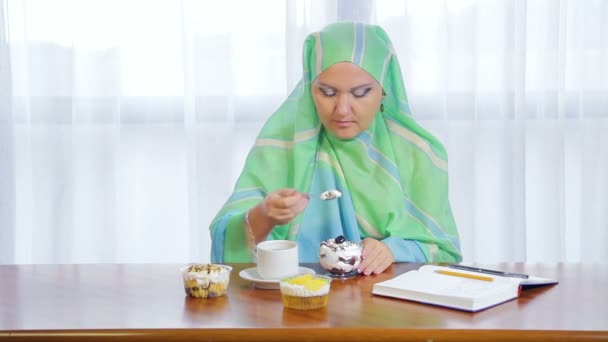 Eine junge muslimische Frau mit leichtem Schal in einem Café isst Kuchen und trinkt Tee — Stockvideo