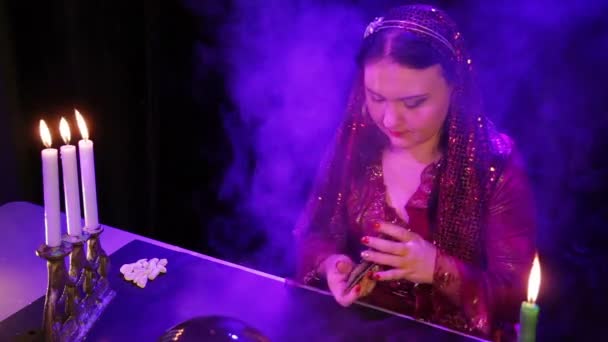 Eine Zigeunerin im roten Kleid im Rauch bei Kerzenschein liest die Zukunft in Karten — Stockvideo