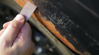 Bir adam bir kazıyıcı ile bir araba gövdesi üzerinde pas temizler