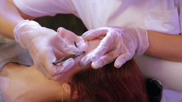The beautician plucks and corrects the clients eyebrows with tweezers. — Stock Video