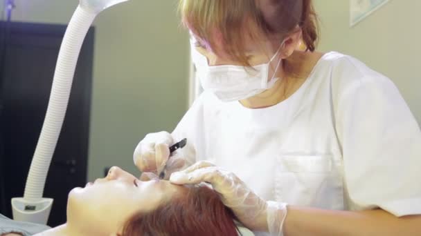 Kosmetikerin korrigiert die Augenbrauen der Kundin mit Pinzette und Pinsel — Stockvideo