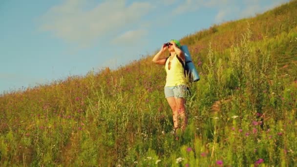 Escursionista donna su una collina con uno zaino dietro di lei, guardando attraverso il binocolo — Video Stock