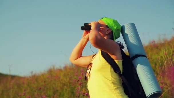 Femme randonneuse sur une colline avec un sac à dos derrière elle, regardant à travers les jumelles à la vue — Video