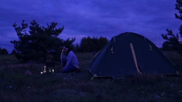 La sera, un uomo e una donna sono alla tenda e un falò frigge carne . — Video Stock