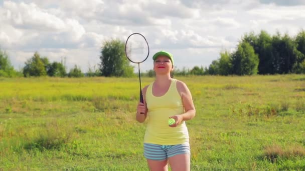 Uma mulher em uma clareira serve e bate a bola ao jogar badminton . — Vídeo de Stock