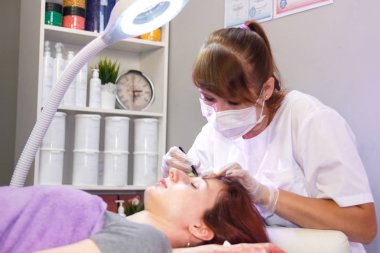 Bir güzellik salonunda bir güzellik cımbız ile bir müşterinin kaşları ayarlar. Yatay fotoğraf