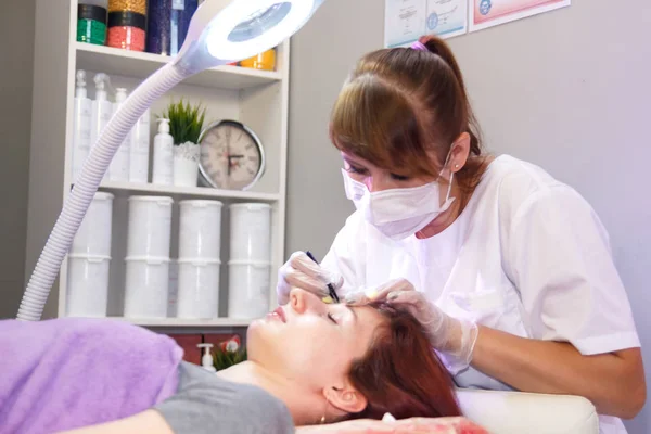 Un esthéticien dans un salon de beauté ajuste les sourcils d'un client avec une pince à épiler. Photo horizontale — Photo