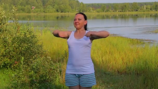 Брюнетка жінка робить вправи на розтяжку на озері вранці — стокове відео