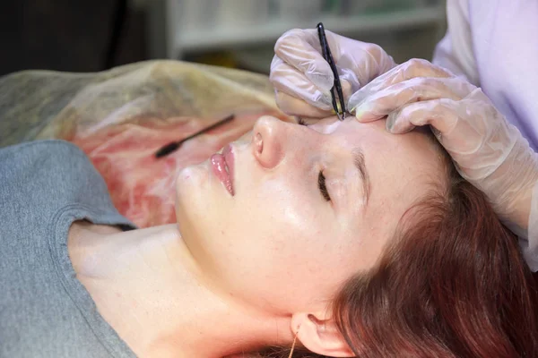 Egy kozmetika egy szépségszalonban beállítja a szemöldökét az ügyfél csipesz — Stock Fotó