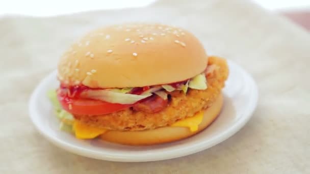 Hamburger s kotlet, rajčaty a sýrem se otáčí v kruhu na bílém talíři. Close-up