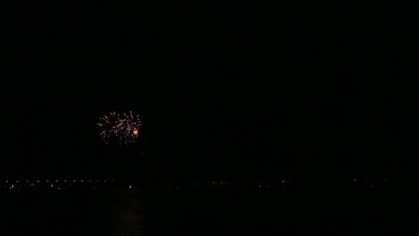 Scintillanti scintille di fuochi d'artificio festivi nel cielo notturno sopra il fiume che si riflettono nell'acqua — Video Stock