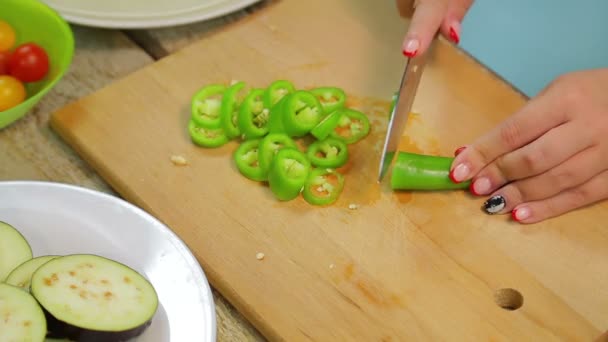 Женщина режет зеленый длинный перец чили с ножом на деревянной доске — стоковое видео