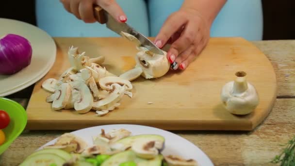 Uma mulher corta os cogumelos champignon em fatias com uma faca em uma tábua de madeira. voltas temporais . — Vídeo de Stock