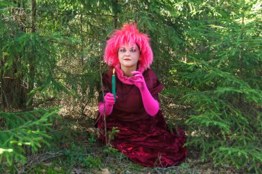 Ormanda elinde bir mum ile mor giysiler içinde genç cadı.