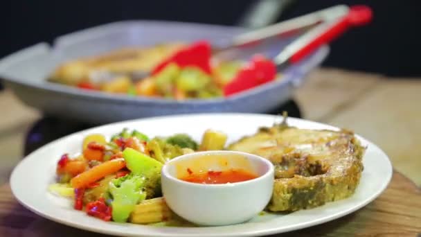 Тарелка спагетти с овощами и рыбой. На заднем плане гриль кастрюля с блюдом . — стоковое видео
