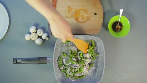 En kvinnans hand rör en stek lök och gröna bönor med en träspatel. — Stockvideo