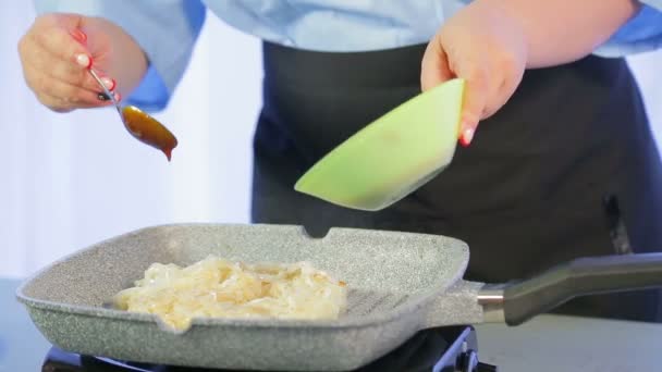 A woman is mixing rice noodles in a frying pan with a wooden spatula — Stock Video