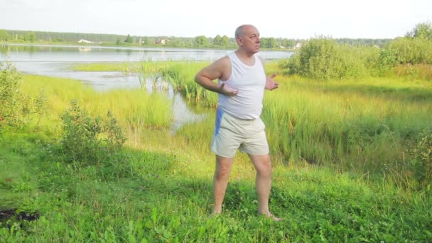 Мужчина средних лет занимается йогой и дыхательными упражнениями на озере утром — стоковое видео