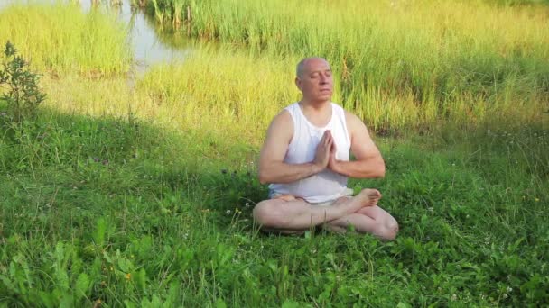 Um homem idoso está envolvido em meditação no lago pela manhã — Vídeo de Stock