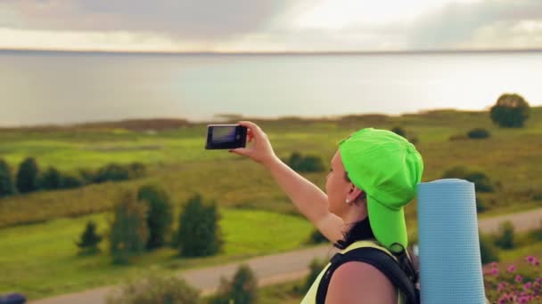 Nő turista egy dombon egy hátizsákot a háta mögött, és távcsövet tesz egy fotót a telefon — Stock videók