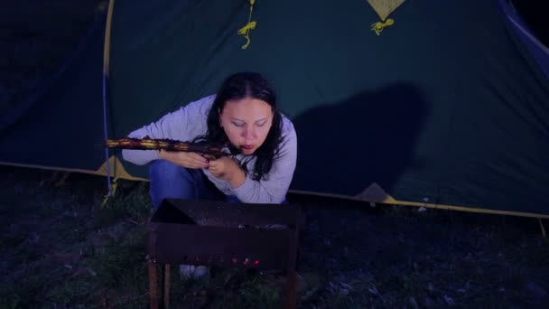Uma mulher em uma tenda e um fogo assam carne e inflam carvão . — Vídeo de Stock