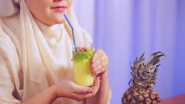 Eine junge muslimische Frau in hellem Schal hält ein Glas mit einem Frucht-Smoothie in der Hand und trinkt aus einem Strohhalm — Stockvideo