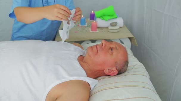 En kvinnlig kosmetolog sätter en återfuktande mask på en mans ansikte — Stockvideo