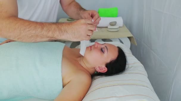 Sameček kosmetolog aplikuje na ženu klienta v lázeňském salónu zvlhčující obličejovskou masku — Stock video