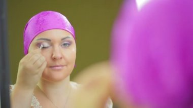 Bir ayna önünde evli bir Jewess bir fırça ile mor gölgeler ile göz makyajı yapar