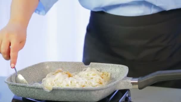 Eine Frau gießt Reisnudeln in eine Pfanne und mischt — Stockvideo