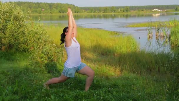 Mulher morena fazendo ioga na pose do herói no lago pela manhã — Vídeo de Stock