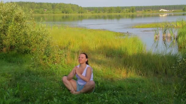 Brunette kvinna gör yoga vid sjön på morgonen — Stockvideo
