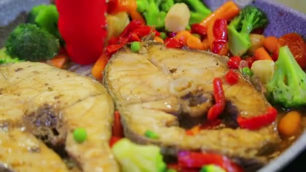 烤架的钳子在平底锅中搅拌蔬菜和鱼烤肉. — 图库视频影像