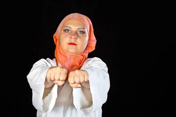 Junge muslimische Frau in Kimono und Schal beim Karatetraining vor schwarzem Hintergrund. Nahaufnahme. — Stockfoto