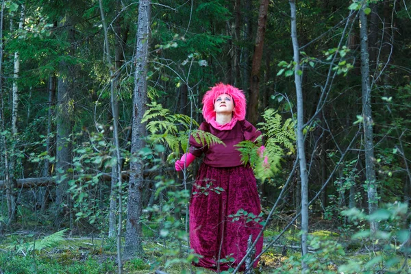 Una joven bruja vestida de púrpura realiza un ritual mágico con un helecho en el bosque . — Foto de Stock