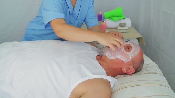 A female beautician puts a moisturizing mask on a mans face — Stock Video