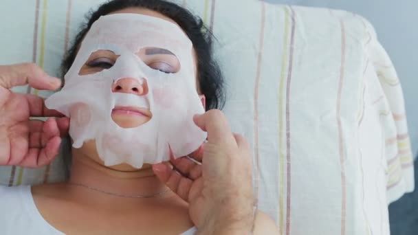 Ένας άντρας αισθητικός εφαρμόζει μια ενυδατική μάσκα προσώπου σε μια γυναίκα πελάτη σε ένα σαλόνι σπα — Αρχείο Βίντεο