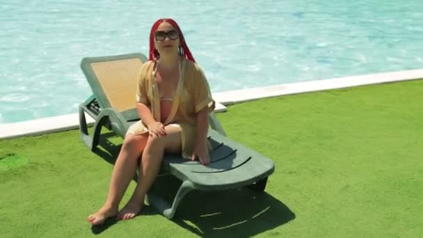 Молода брюнетка купається на стільці біля басейну — стокове відео