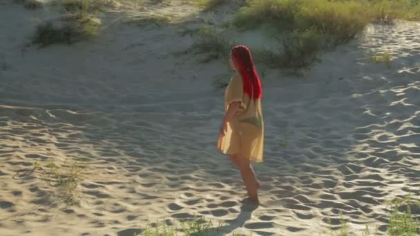 Mayo ve bornozlu bir kadın sahilde kumda yalınayak yürüyor. — Stok video