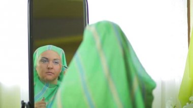 Müslüman kadın aynaya yansıyan parlak gölgeler ile göz makyajı yapar