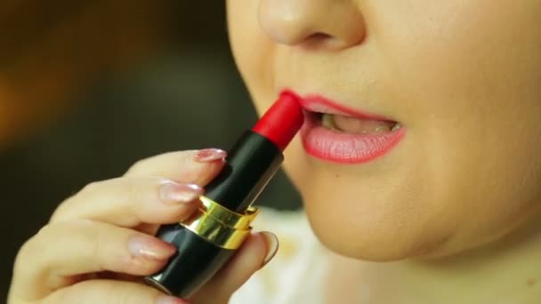 Een vrouw voor een spiegel schildert haar lippen met rode lippenstift — Stockvideo