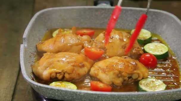 Main féminine tourne des morceaux de légumes avec pinces et poulet sur une poêle à griller — Video